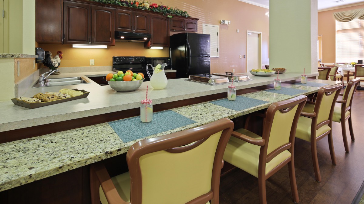 A modern kitchen with a granite counter, equipped with chairs and fruit bowl.