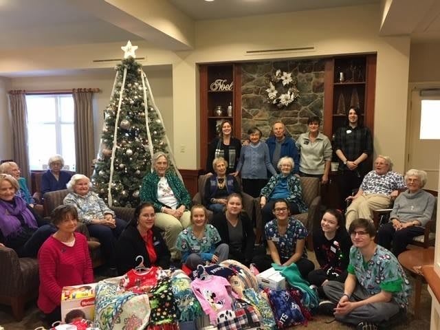 A group of people gathered around a Christmas tree with gifts, celebrating the holiday indoors.