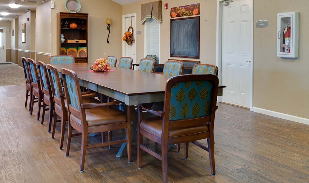 A cozy dining room with a large wooden table, surrounded by chairs, decorated with autumn-themed ornaments.