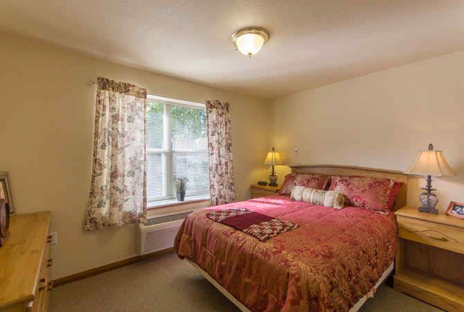 A cozy bedroom with a bed, lamp, and window with floral curtains.