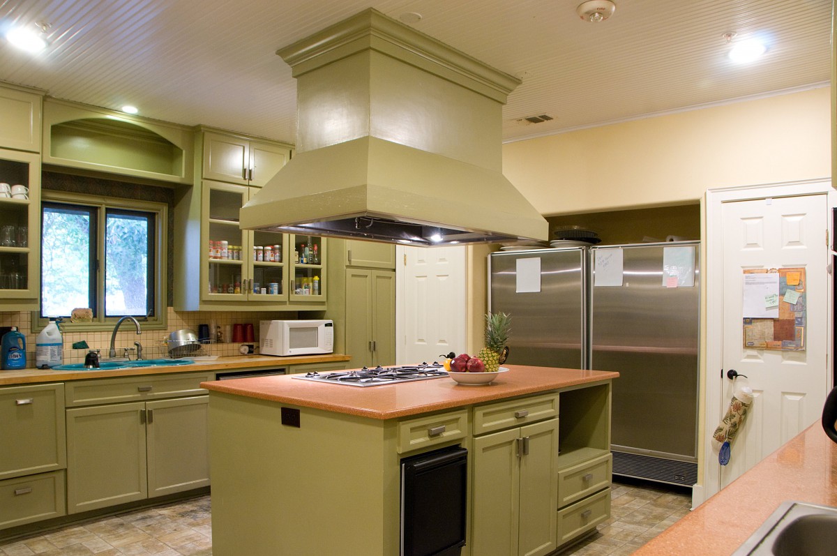 A modern kitchen with green cabinets, a central island with a stove, and stainless steel fridge.