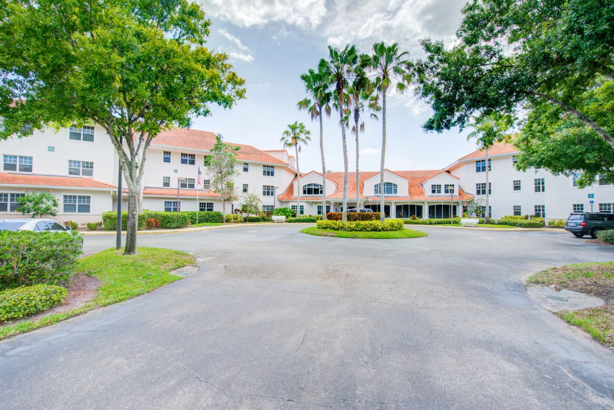 A residential building with palm trees and a circular driveway on a clear day.