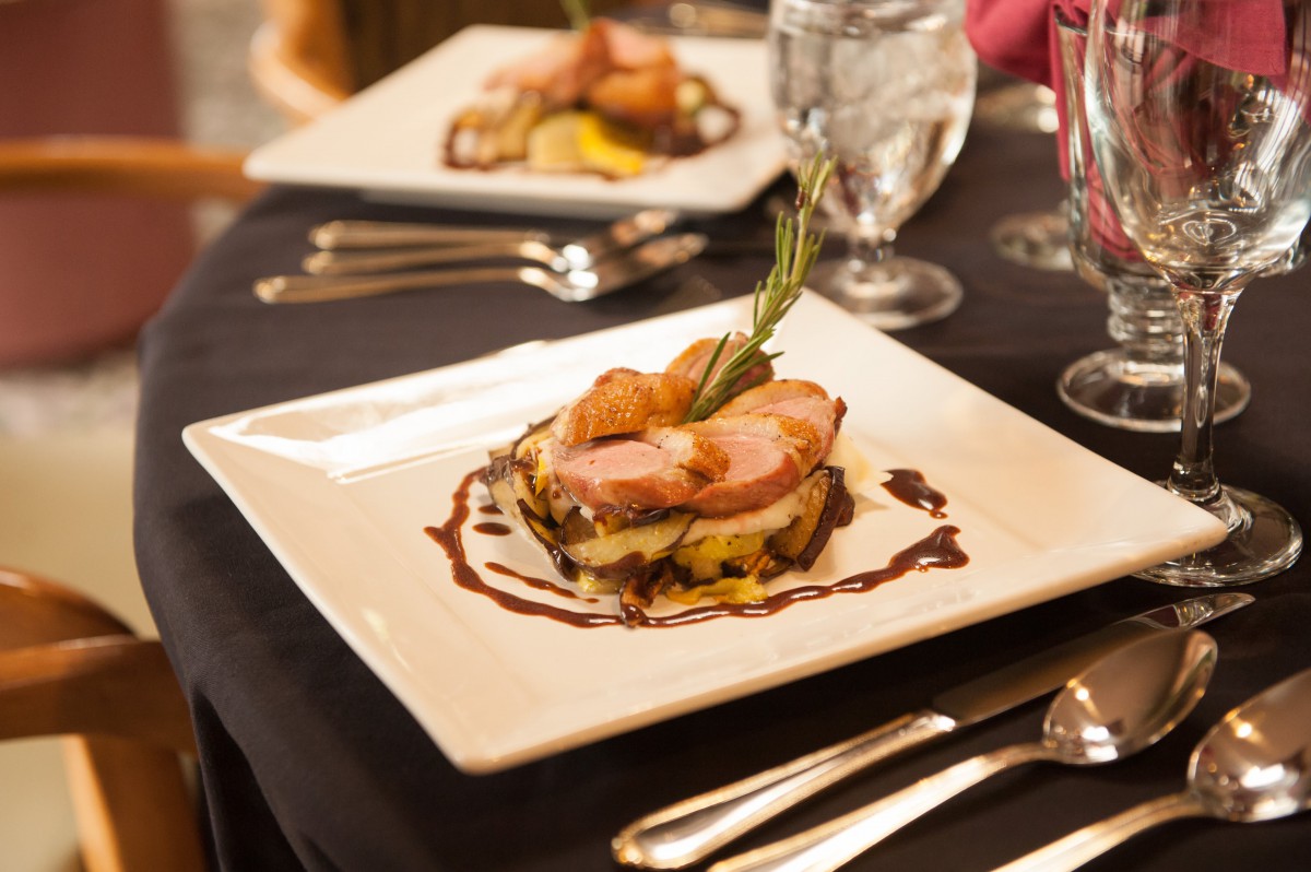 A beautifully presented gourmet dish served on a square white plate, accompanied by elegant table settings.