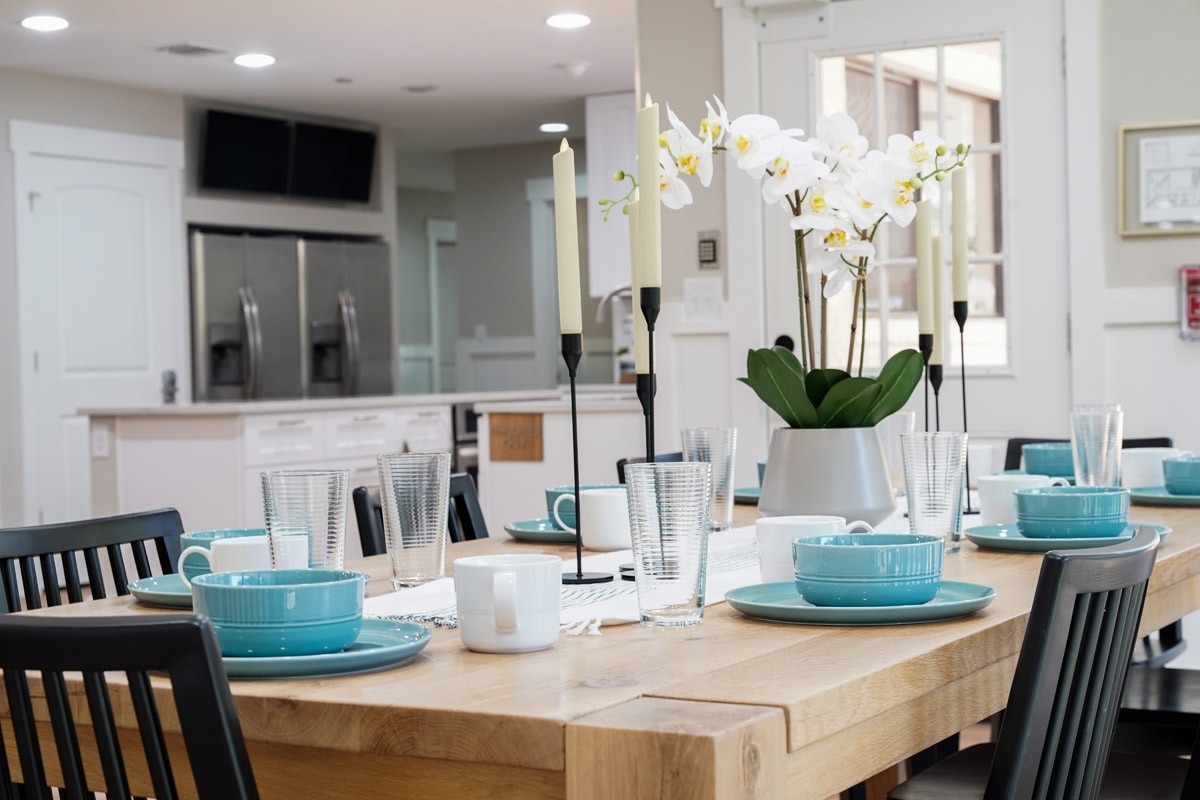 A modern dining table set with turquoise dishes, candles, and a potted orchid centerpiece.