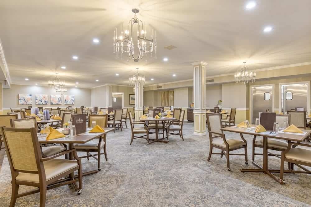 An elegant dining room with neatly arranged tables and chairs, featuring chandeliers and soft lighting.