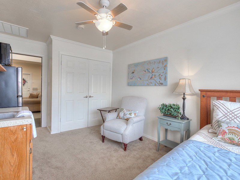 A cozy bedroom featuring a comfortable armchair, a bedside lamp, and a ceiling fan.