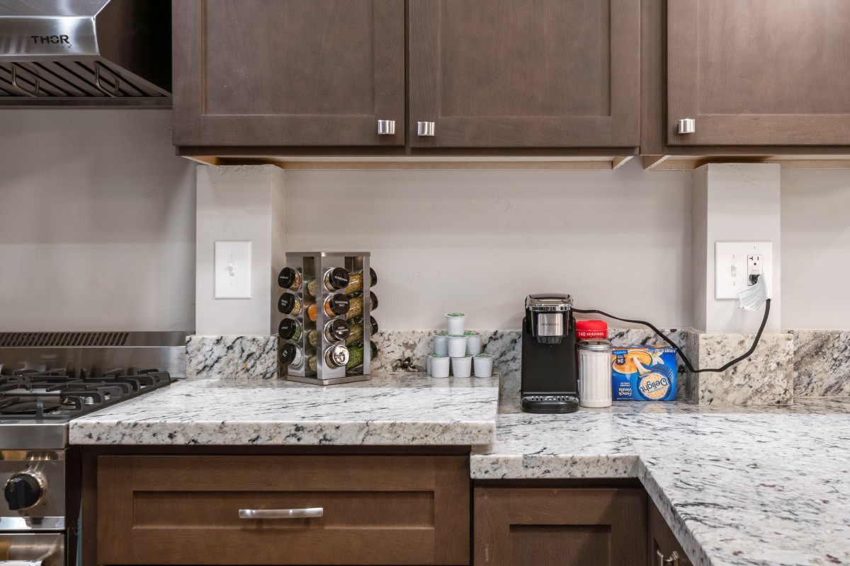 A kitchen counter with a coffee maker, spice rack, and marble countertop.