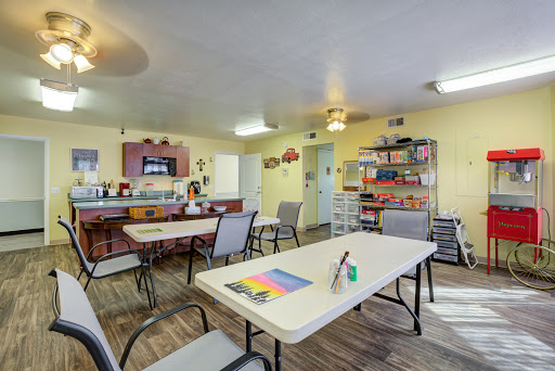 A bright and welcoming community room equipped for activities, featuring tables, chairs, and art supplies.