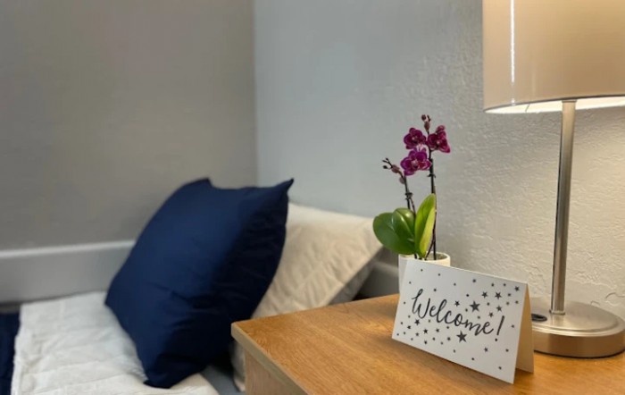 A cozy bedroom setup featuring a welcome sign and a vibrant orchid on a bedside table.
