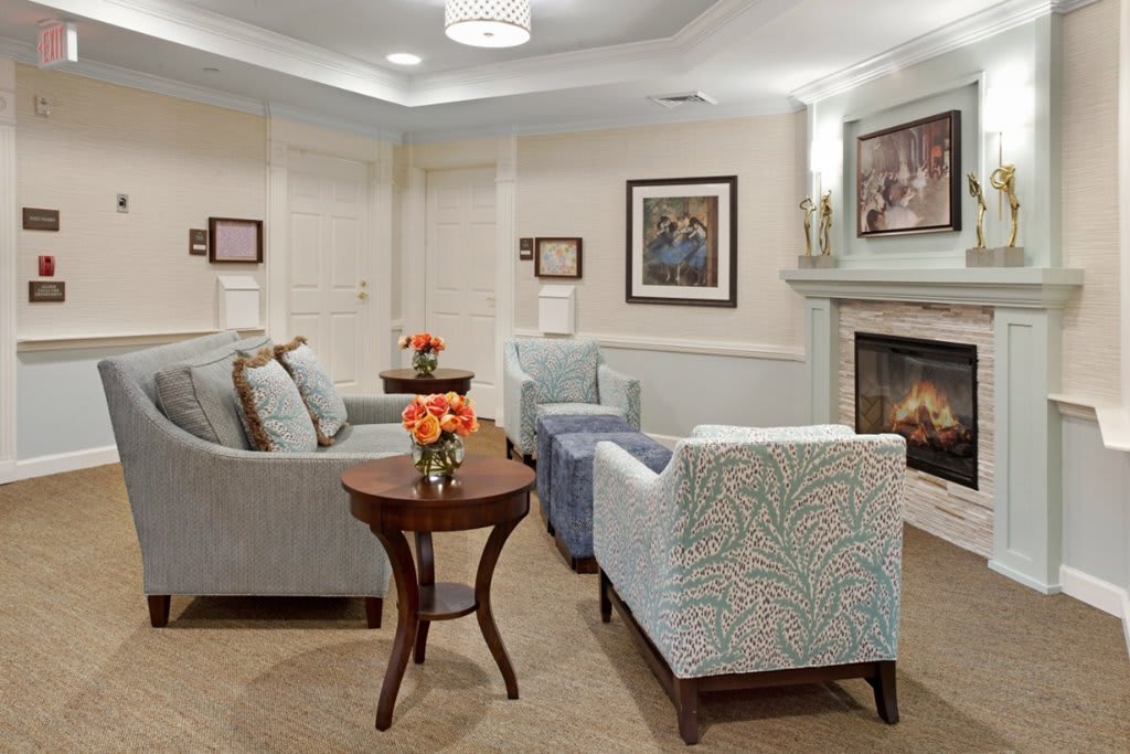 A cozy living room with sofas, chairs, a table, and a fireplace adorned with artwork.