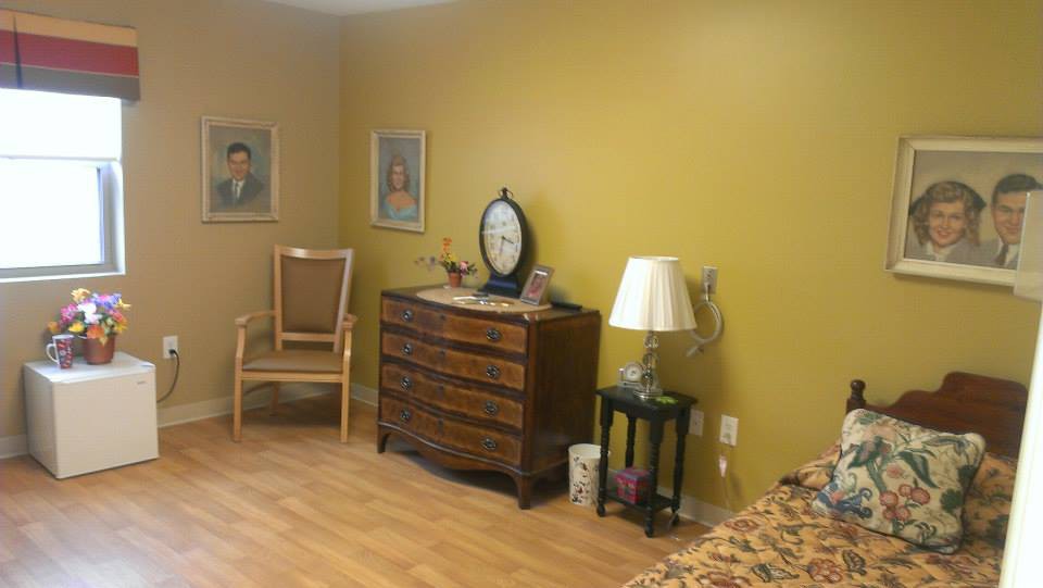 A cozy bedroom with a wooden dresser, chair, and artwork on mustard-colored walls.
