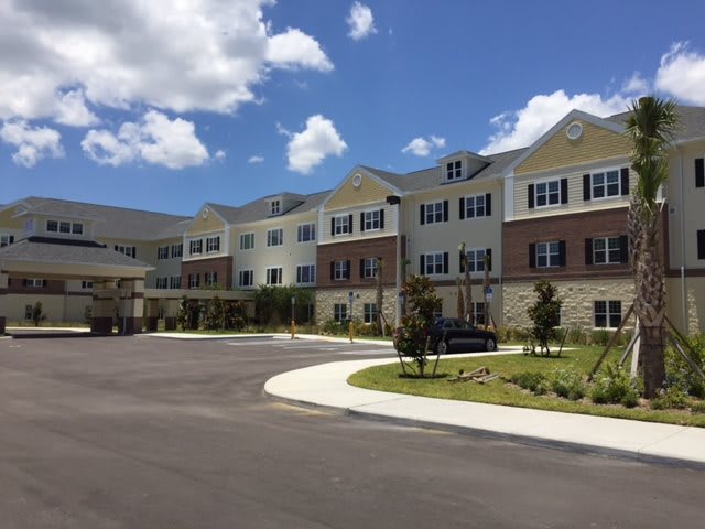 A modern residential building with a well-maintained parking lot and landscaping under a partly cloudy sky.