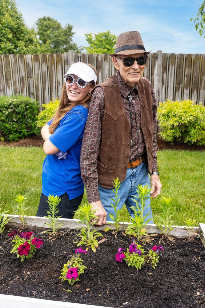 Two people pose happily in a garden with a planter box full of flowers.