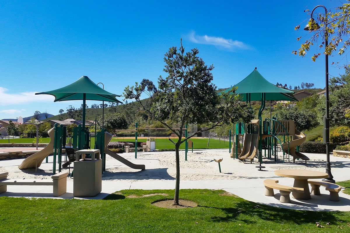 A sunny day at a vibrant outdoor playground with swings, slides, and lush greenery.