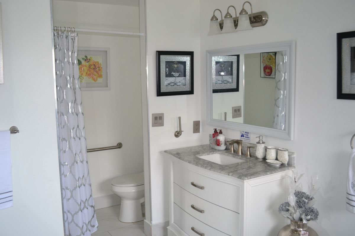 A modern white bathroom featuring a vanity with a mirror, shower curtain, and neatly arranged toiletries.