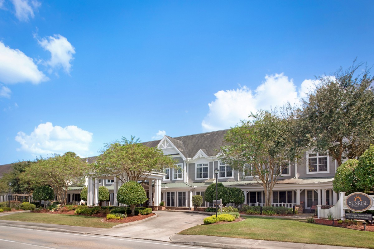 A large residential building surrounded by trees under a clear blue sky.
