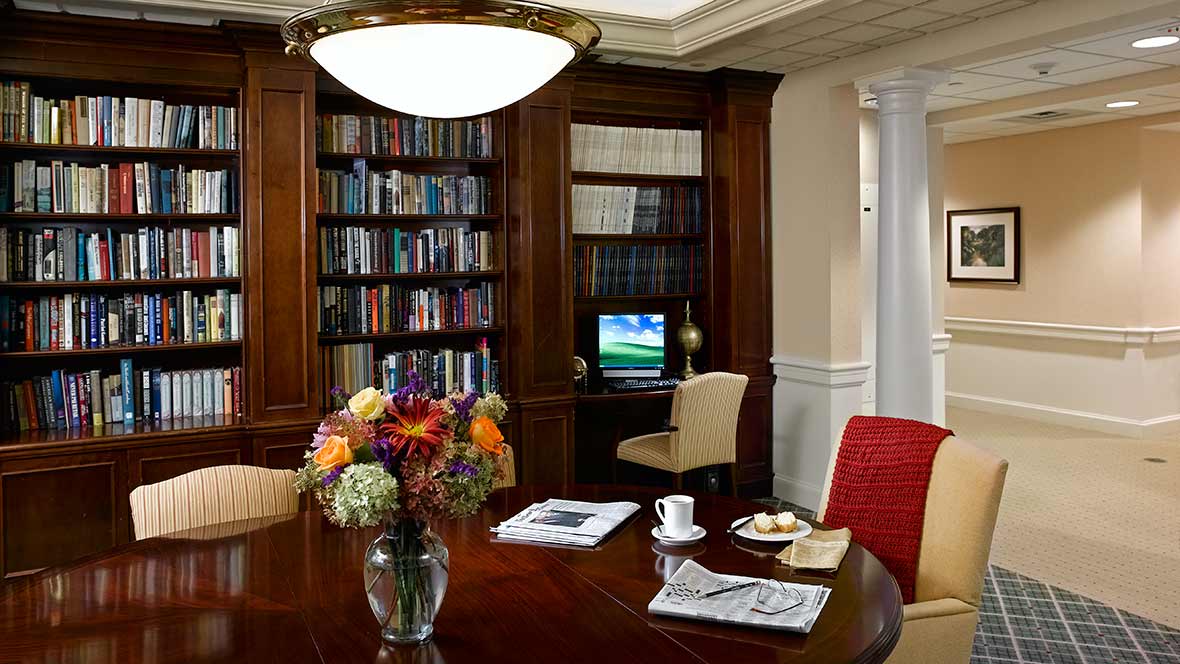 A cozy library corner with bookshelves, a computer, and a table adorned with flowers.
