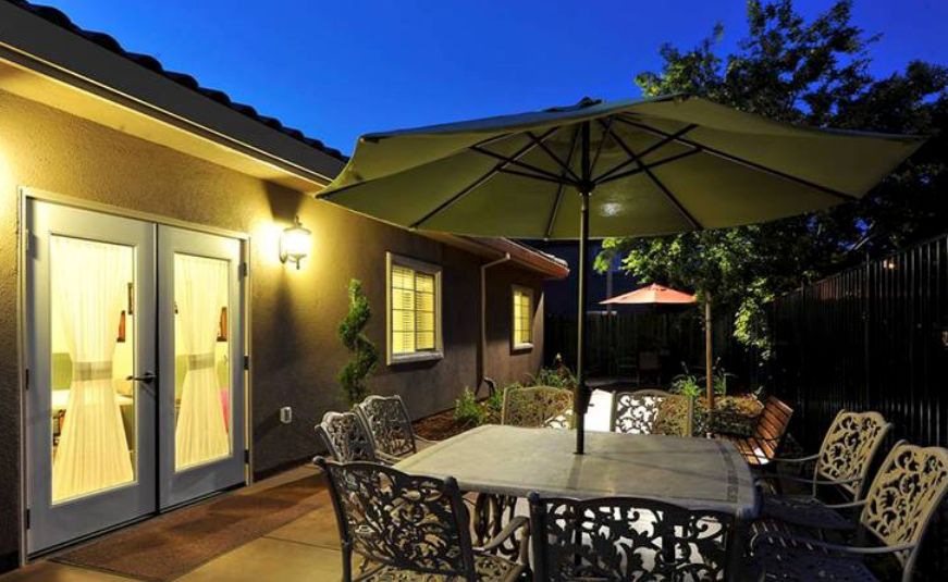 A cozy patio area with a table and umbrella set against the evening backdrop of a well-lit house exterior.
