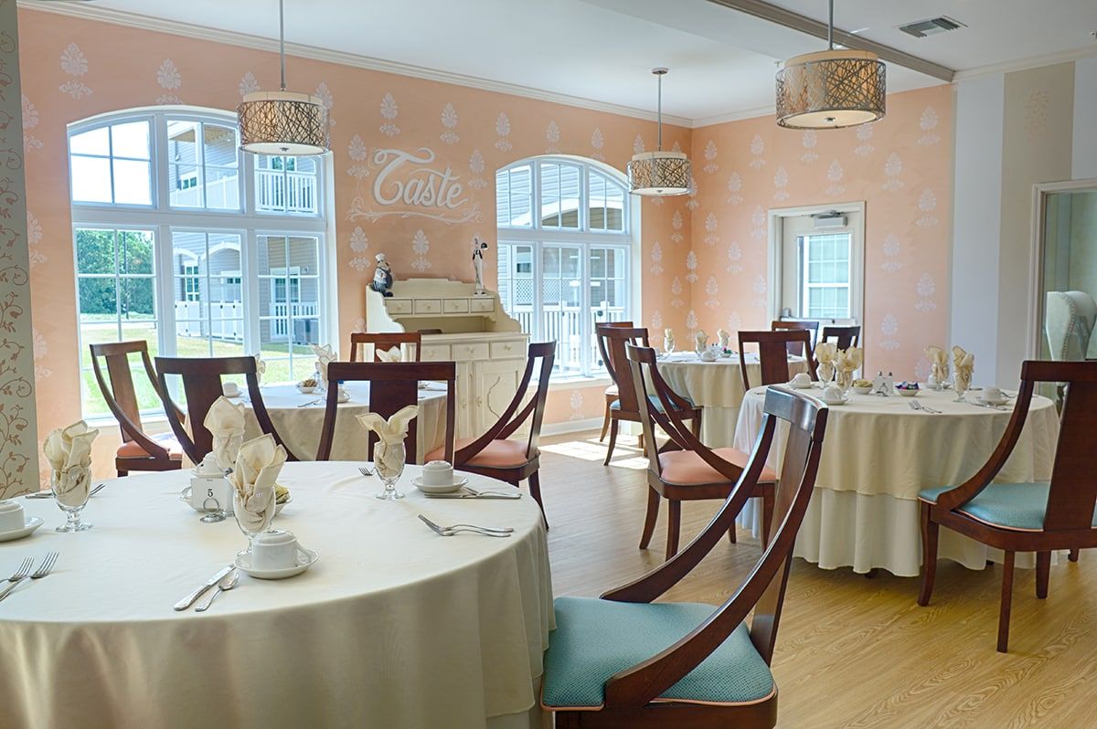 An elegant dining room with round tables, wooden chairs, and soft lighting.