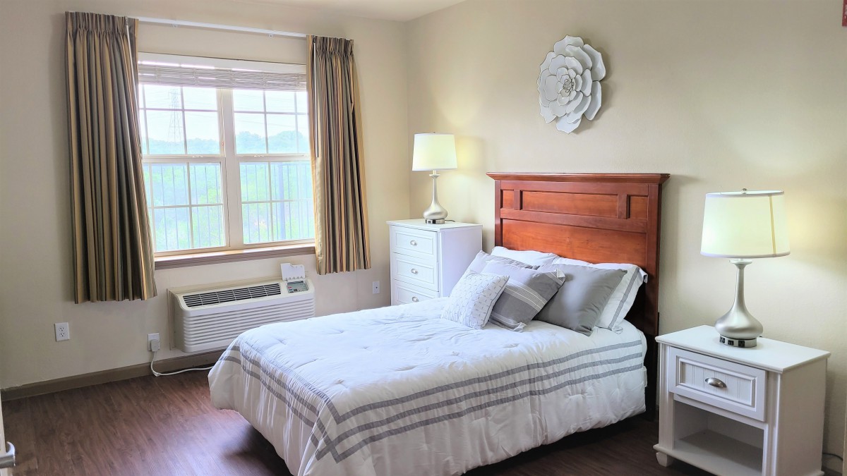 A cozy bedroom with a neatly made bed, large window, and stylish decor.