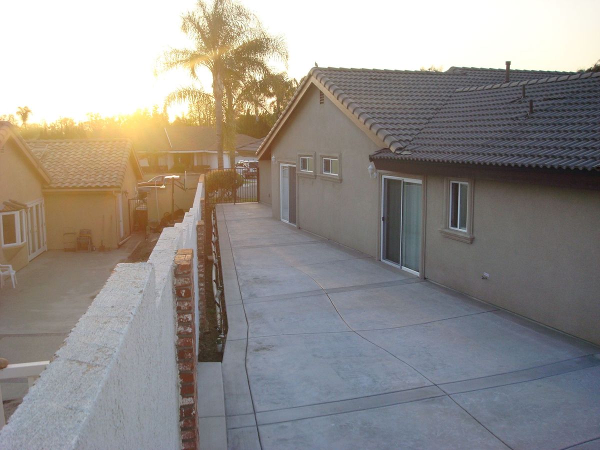 A residential house with a paved driveway during sunset, featuring a palm tree in the background.