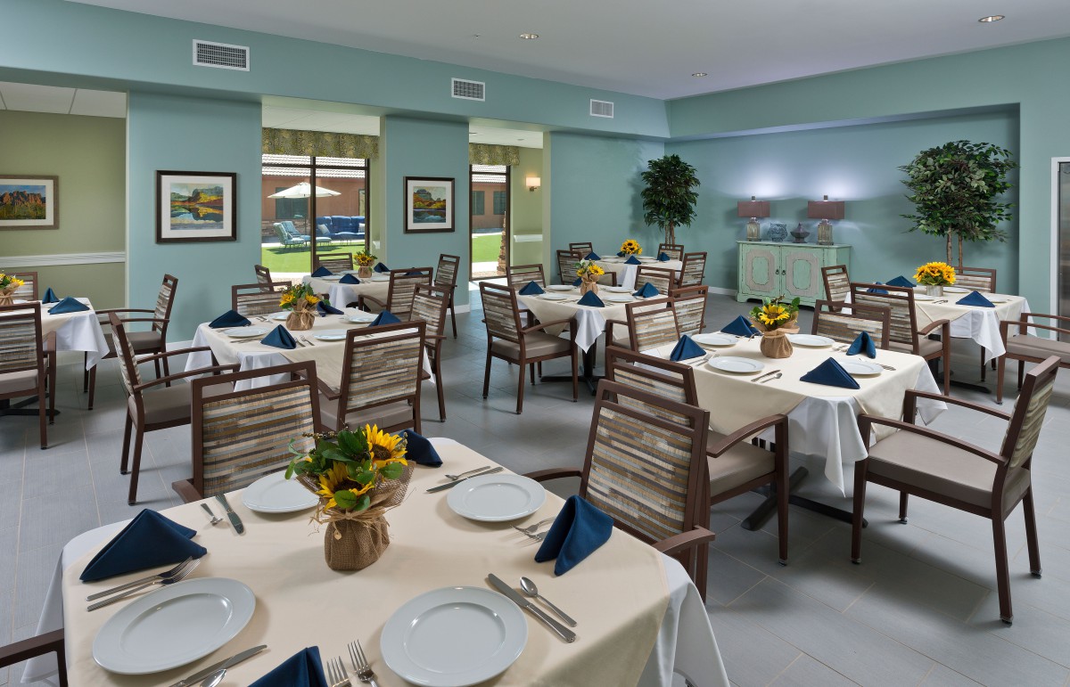 A spacious dining room with elegantly set tables and chairs, adorned with flowers and neatly folded napkins.