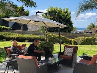 A sunny day on the patio with people relaxing under an umbrella.