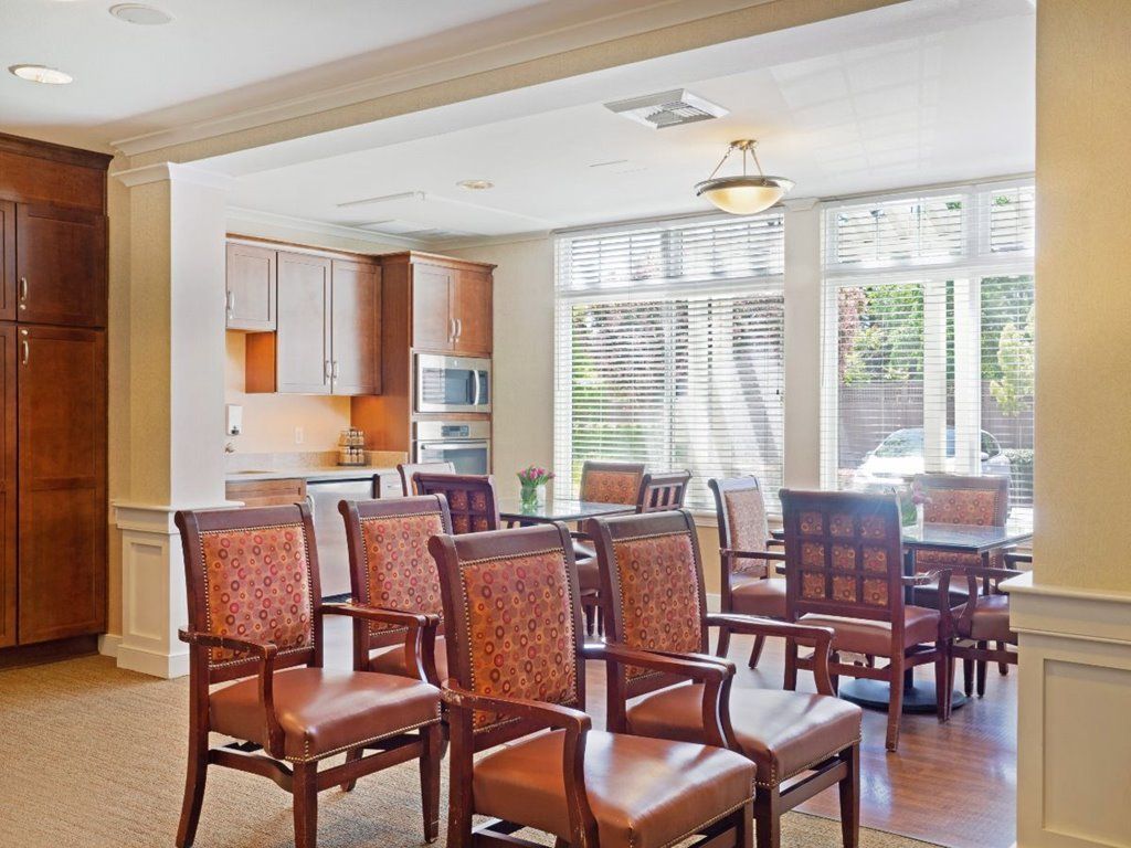 A cozy dining area with wooden chairs and a table, adjacent to a kitchen with modern appliances.