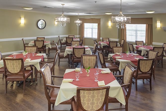 A well-arranged dining room with tables and chairs set for a meal, featuring elegant chandeliers.