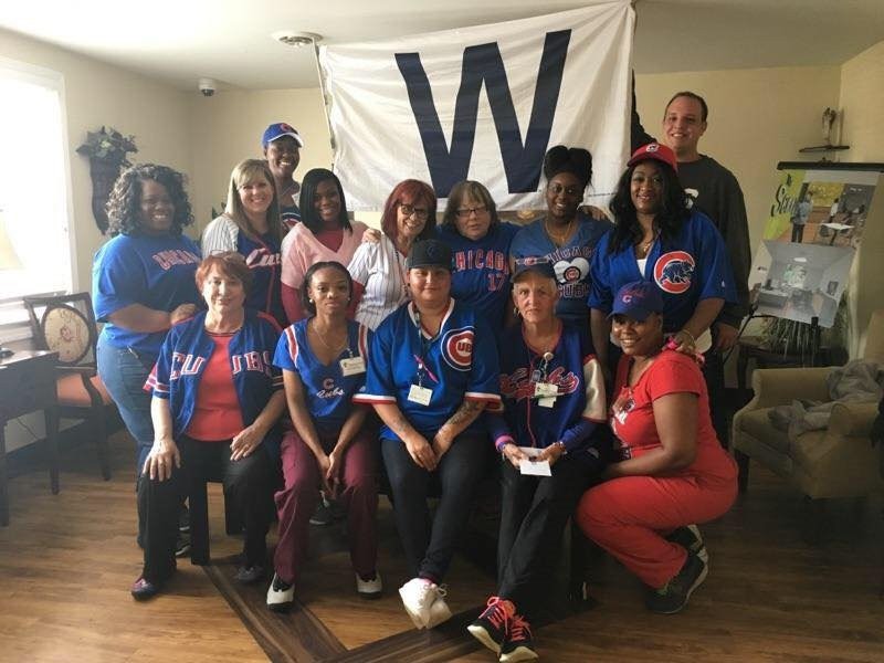 A group of people celebrating, wearing Cubs jerseys and posing in front of a large 'W' flag.
