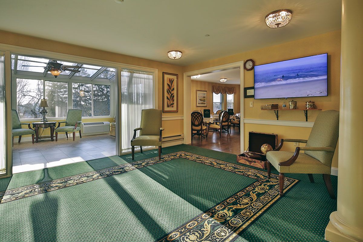A cozy living room with a television, chairs, and large windows allowing natural light.