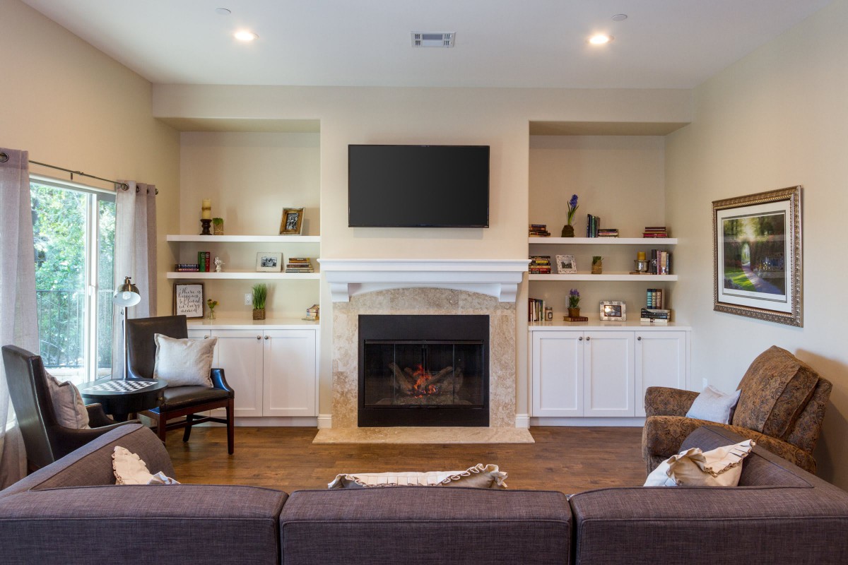 A cozy living room with a fireplace and built-in shelves, featuring a mounted TV above the mantel.