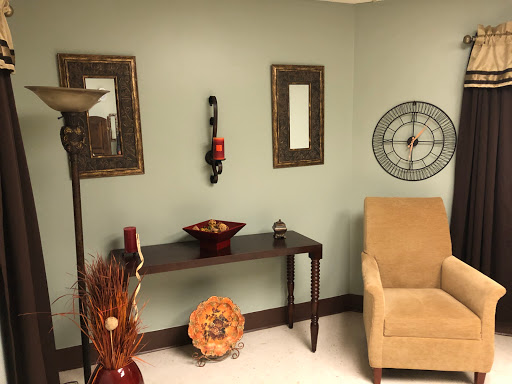 A cozy corner of a room featuring a light green wall, decorative frames, a stylish lamp, and elegant furniture.
