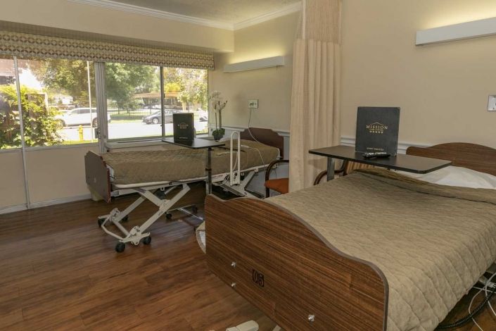 A hospital room with two patient beds and medical equipment, featuring large windows and a clean, organized environment.