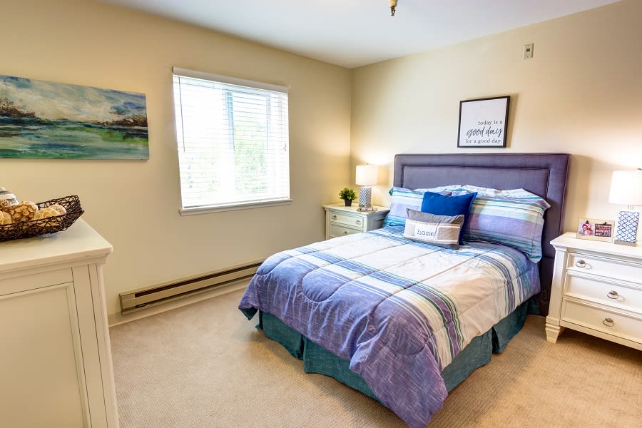 A cozy bedroom with a neatly made bed, bedside table, and window letting in natural light.