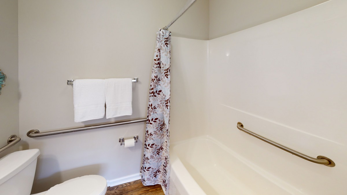 A clean bathroom with a bathtub, floral shower curtain, and neatly hung towels.