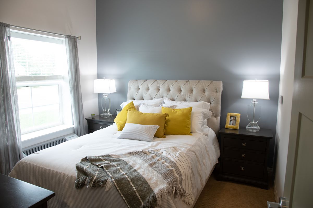 A cozy bedroom with a tufted headboard, yellow accent pillows, and matching lamps on dark nightstands.