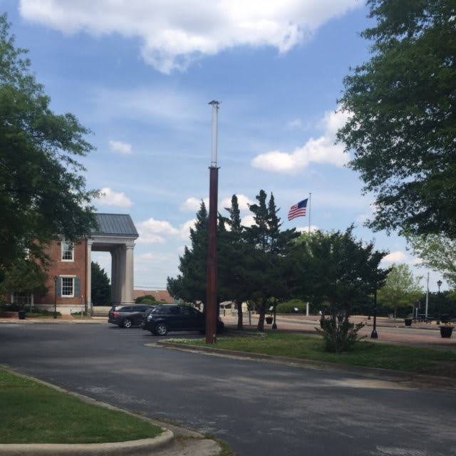 A view of a building with a parking lot, surrounded by trees and a flagpole under a partly cloudy sky.