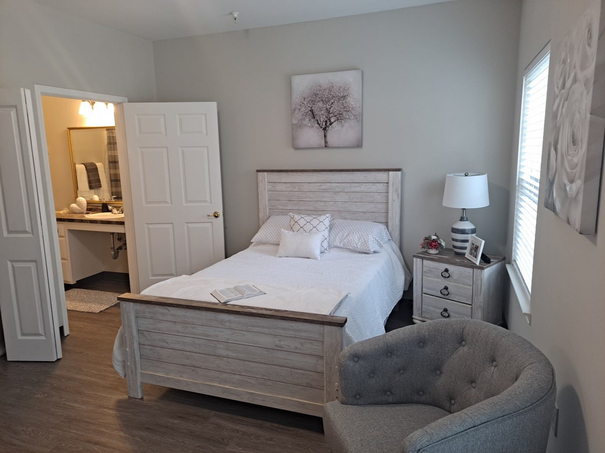 Cozy bedroom with white decor, featuring a bed, nightstand, and a comfortable armchair.