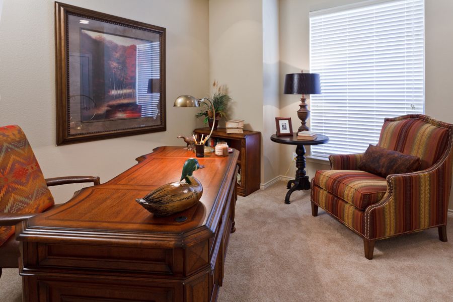 A cozy home office with a wooden desk, comfortable armchair, and soft lighting.