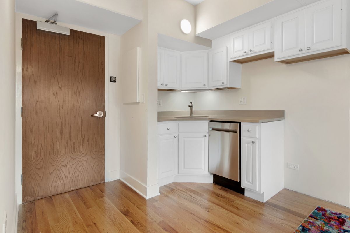 A modern apartment kitchen with white cabinets and stainless steel appliances.