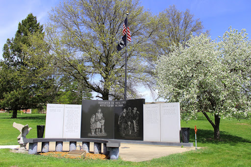 A veterans memorial featuring a flag and etched images of soldiers, surrounded by trees in a serene outdoor setting.