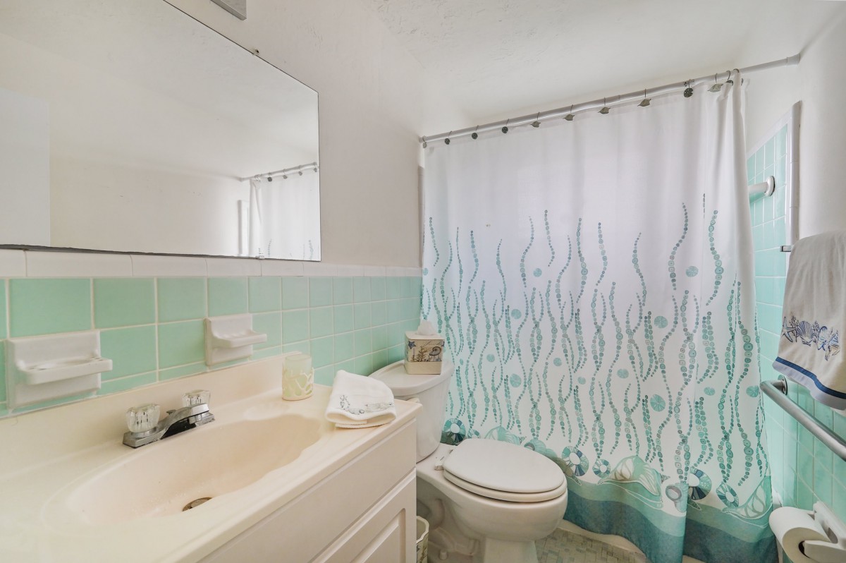 A clean bathroom with green tiles, featuring a sink, toilet, and a decorative shower curtain.