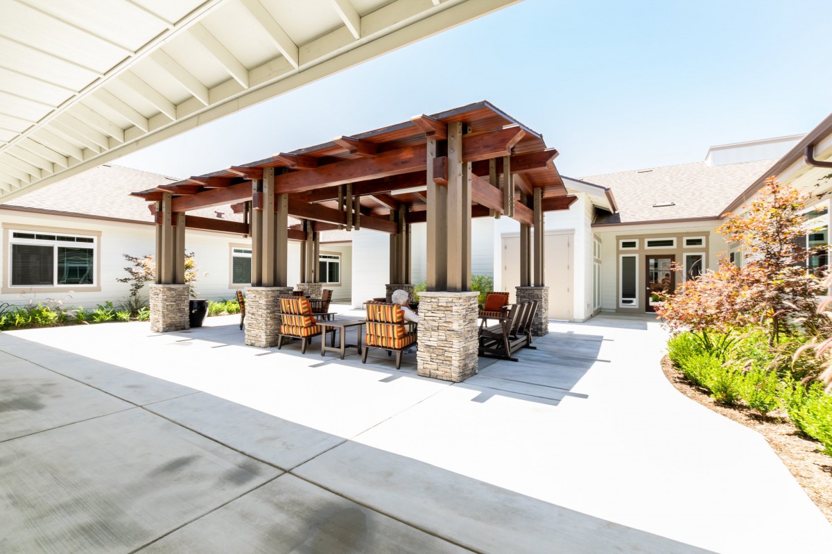 A modern outdoor patio with a pergola, featuring comfortable seating and stone column support on a sunny day.