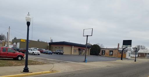 An empty basketball hoop stands near a building on a cloudy day.
