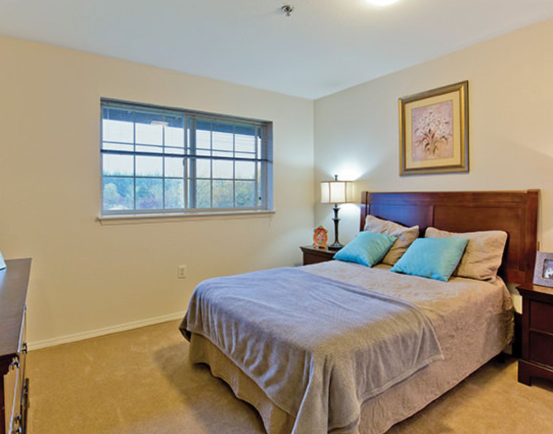A cozy bedroom with a neatly made bed, soft lighting, and a window view.