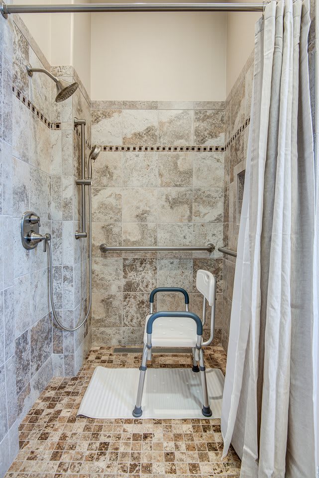 An accessible bathroom with a shower chair and grab bars for safety.