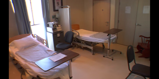 A view of a hospital room with a bed, chair, and medical equipment.
