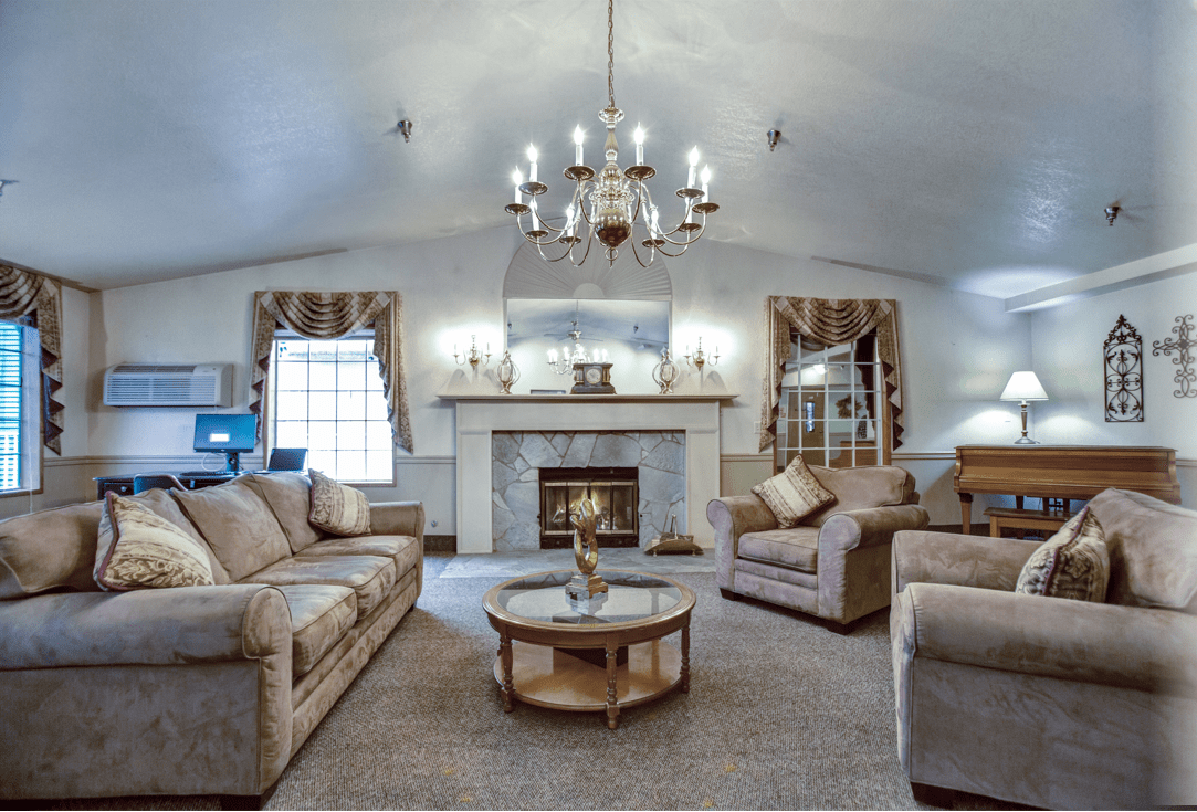 A cozy living room with comfortable sofas, a central coffee table, and a chandelier illuminating the space. The fireplace adds warmth, while elegant curtains frame the windows.