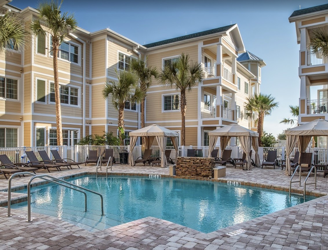 A luxurious resort with a sparkling outdoor pool surrounded by palm trees and elegant buildings.